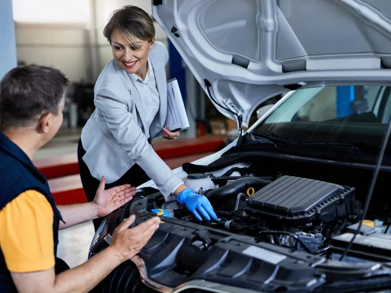 auto mechanic businesswoman cooperating while checking vehicle hood workshop